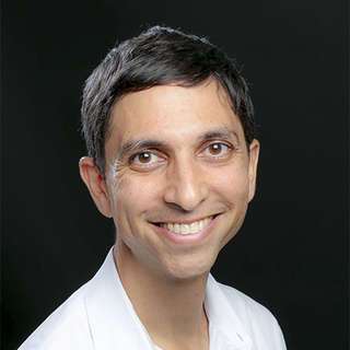 Dr. Onil Bhattacharyya, seen form the shoulders up, wearing a white lab coat, short black hair, and smiling