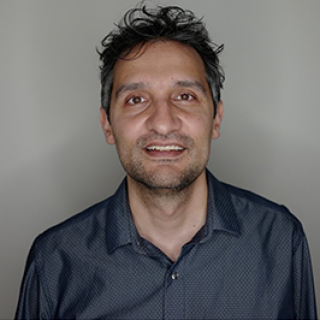 Omar Khan, seen from the chest up, wearing a grey button up, short black hair, and smiling