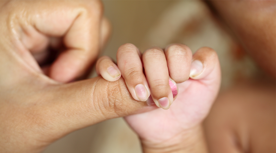 a newborn holds the thumb of an adult