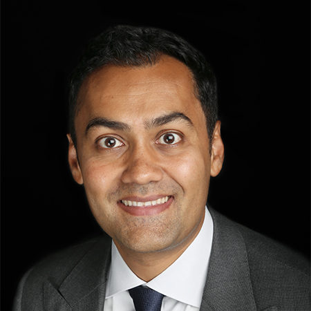 Sacha Bhatia, seen from the shoulders up, wearing a grey suit and tie, smiling