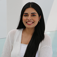 Sarah Qureshi, seen from the chest up, wearing a white blouse, long black hair, and smiling
