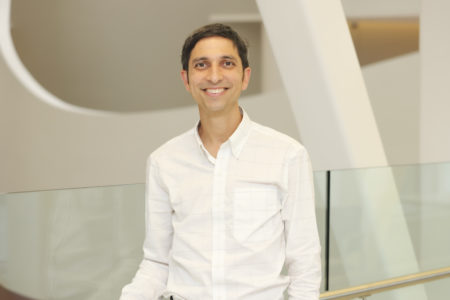 Dr. Bhattacharyya, seen from the waist up, wearing a white collared shirt, short brown hair, and smiling